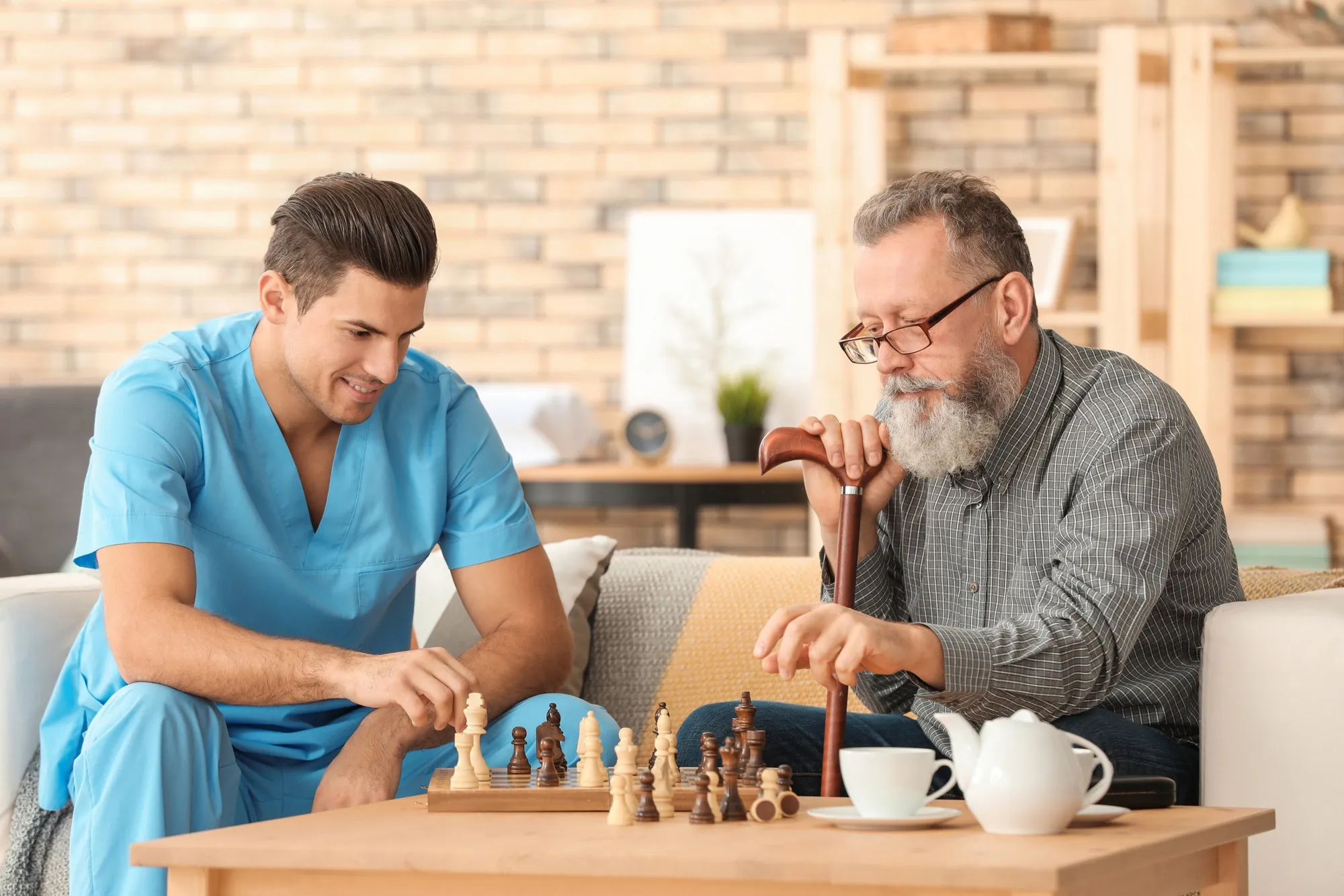 A caregiver and an older man playing chess at home.